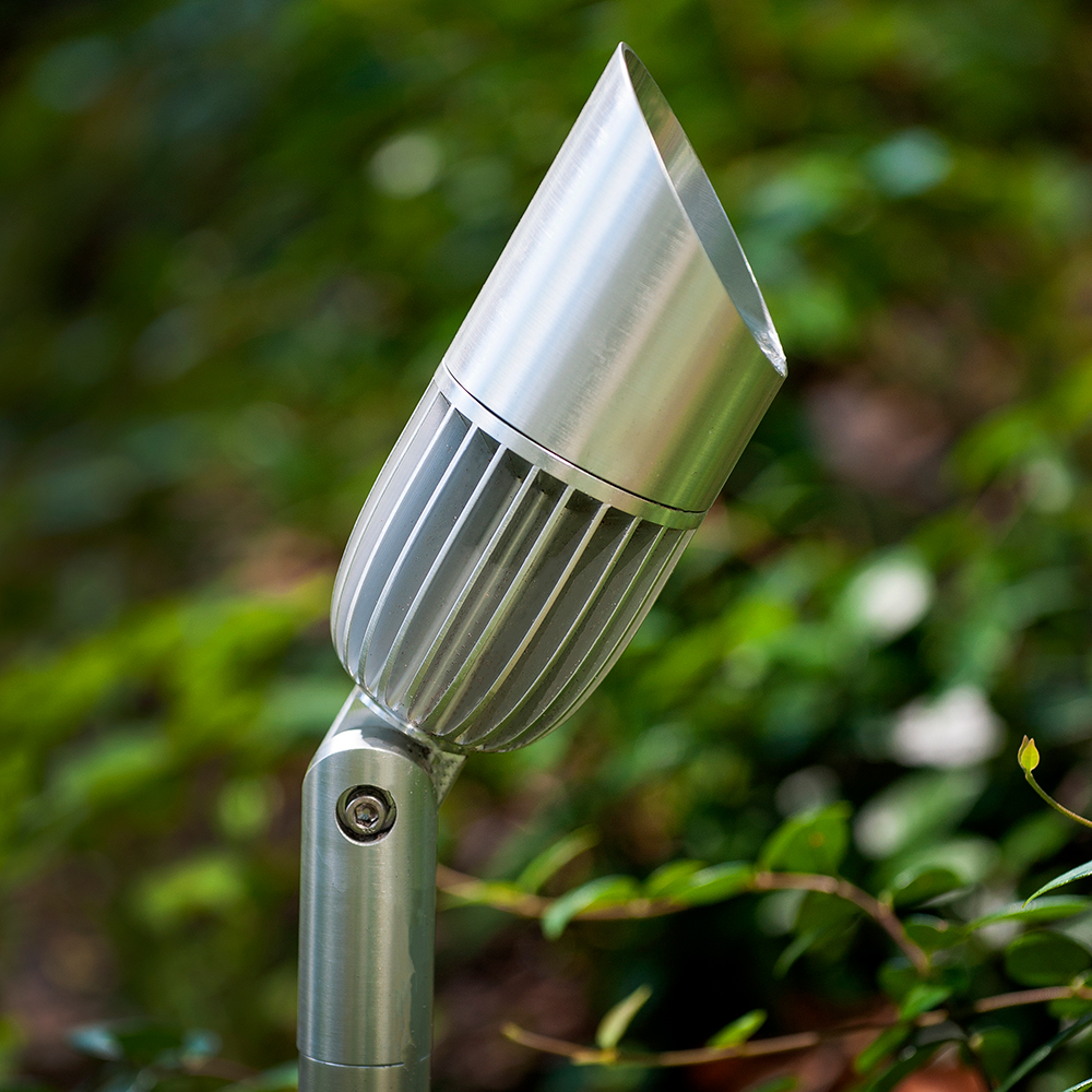V3 Spotlight installed in a planting bed with stainless finish and visible heat-sink finning